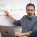 Software developer and educator explaining JavaScript concepts on a whiteboard, pointing to a flowchart showing input, validation, transformation, and return steps while a laptop with code sits open on the desk.